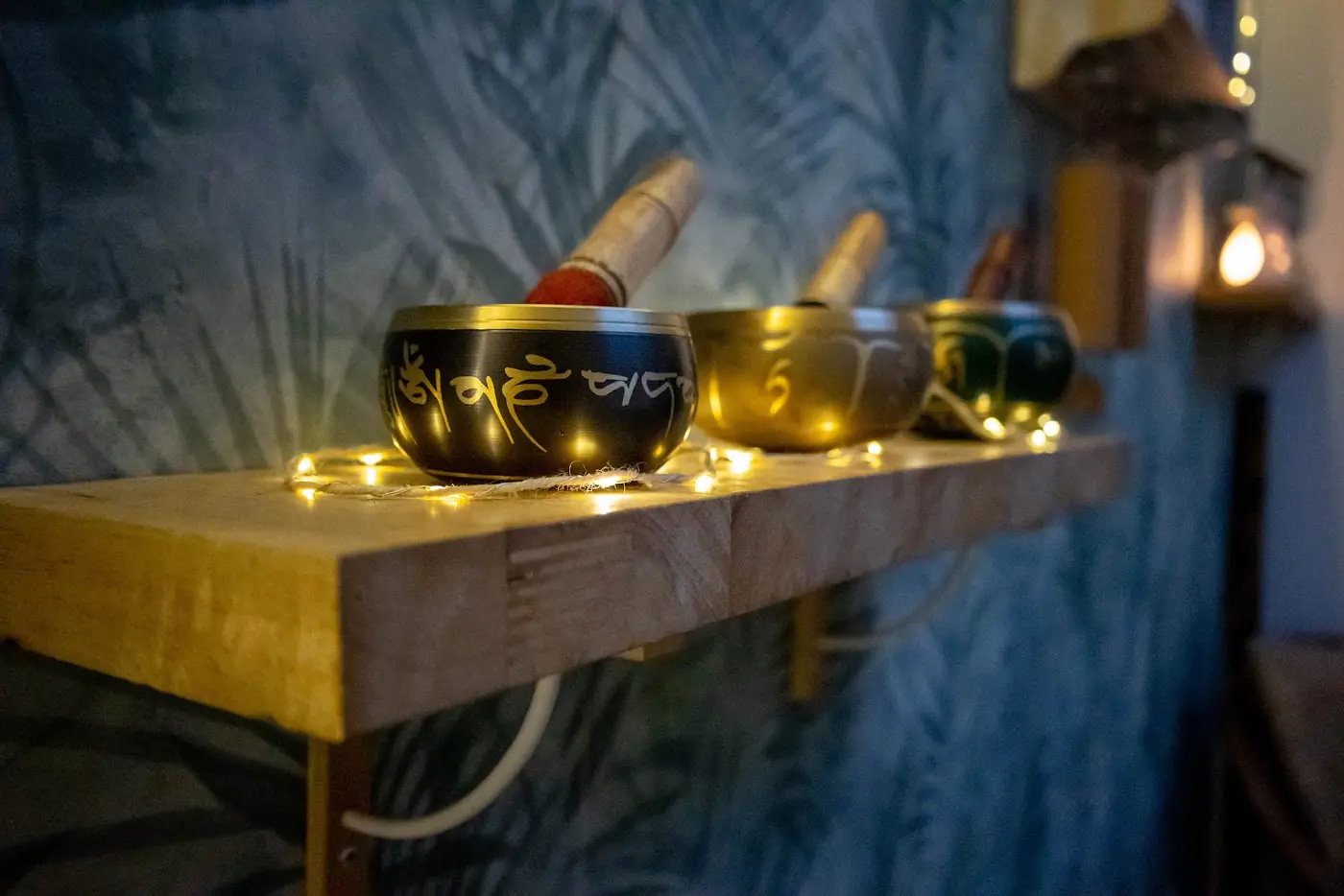 Trois bols chantants alignés sur une étagère en bois, avec une guirlande lumineuse